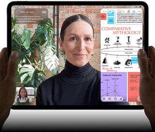 iPad Pro, front exterior, landscape orientation, space black color, rounded corners, black display bezel, hands holding left and right sides, display showing a FaceTime conversation being live translated, and an educational app showing a presentation of "Comparative Mythology" with text, diagrams, and handwritten notes