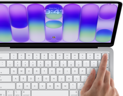 MacBook Neo, silver color, showing login screen, person's finger on Touch ID sensor in top-right corner of keyboard
